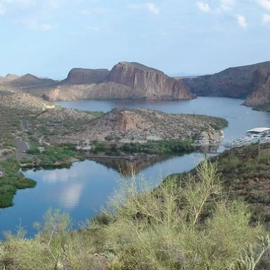 A scenic desert lake surrounded by rugged hills under a partly cloudy sky.
