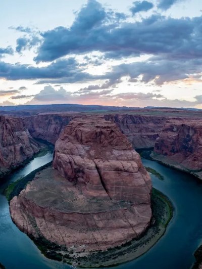Scenic view of Horseshoe Bend with river and rocky cliffs beneath a dramatic cloudy sky.