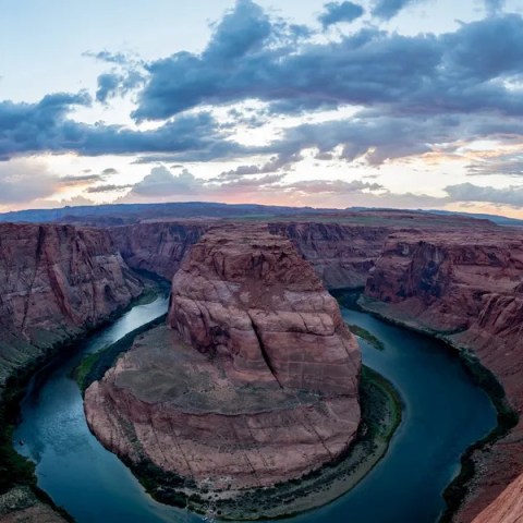 Scenic view of Horseshoe Bend with river and rocky cliffs beneath a dramatic cloudy sky.