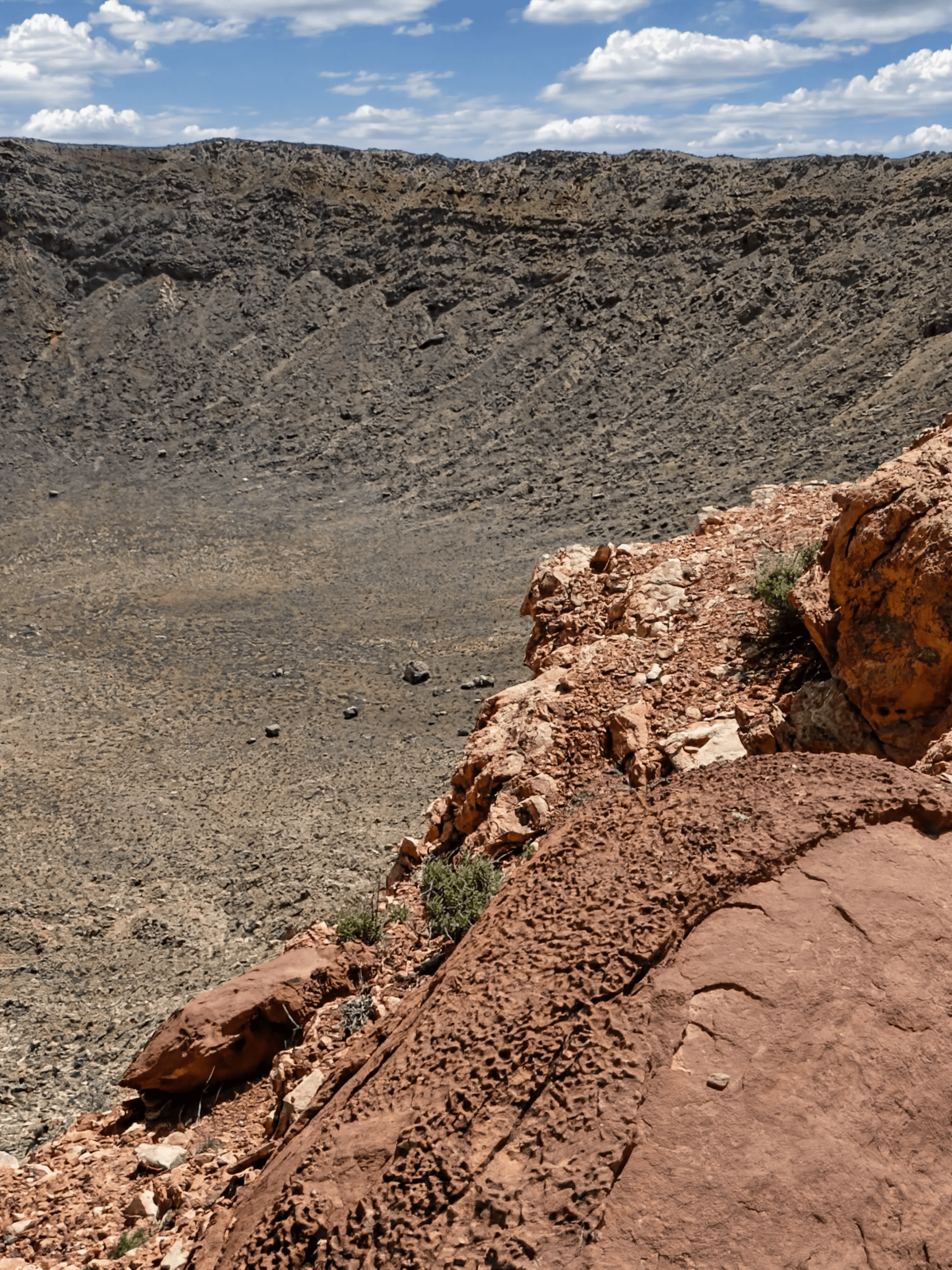 Rocky desert landscape with large crater under a partly cloudy sky.