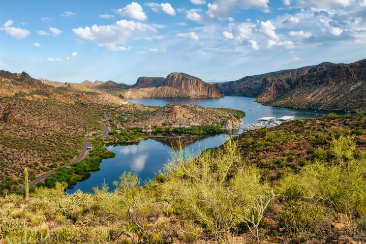 Scenic view of a lake surrounded by desert landscape and hills under a partly cloudy sky.