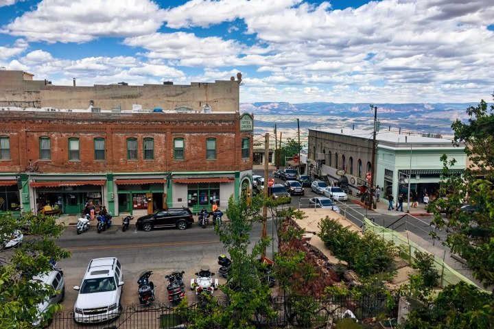 Street view of historic town with parked vehicles and people on a partly cloudy day.