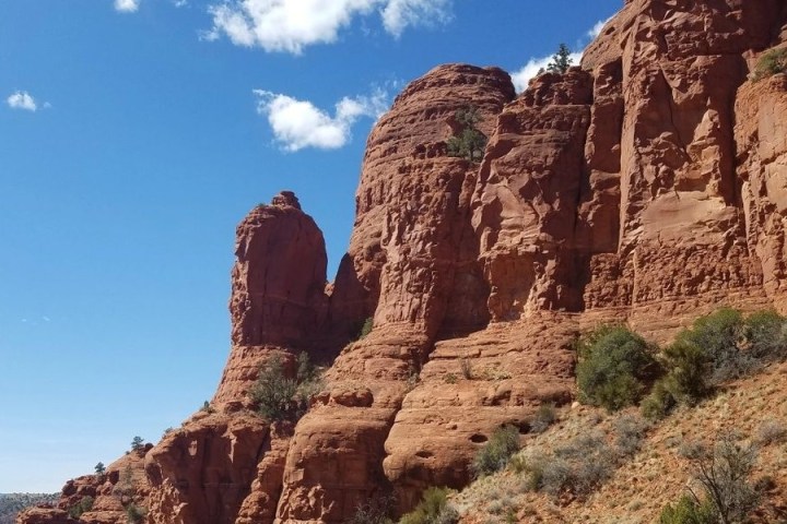 Red rock formations under a clear blue sky with sparse greenery.