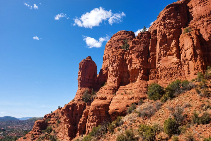 Red rock formations under a clear blue sky with sparse clouds.