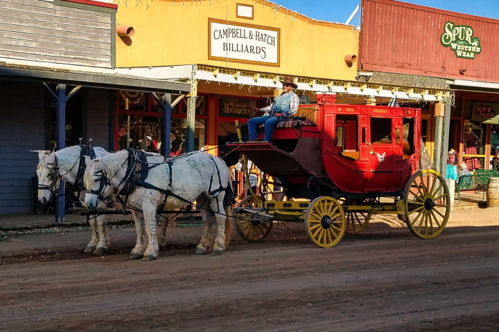 Horse-drawn stagecoach on a dirt street in a western town scene.