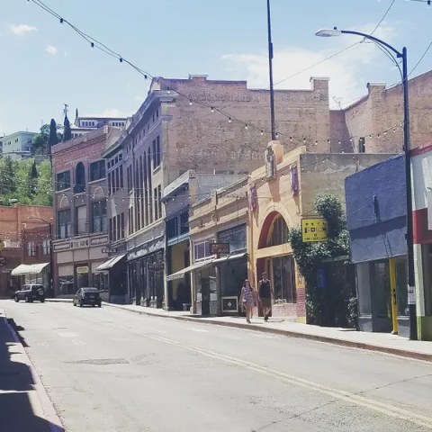 Sunny street with historic buildings, Italian flag, and two people talking.