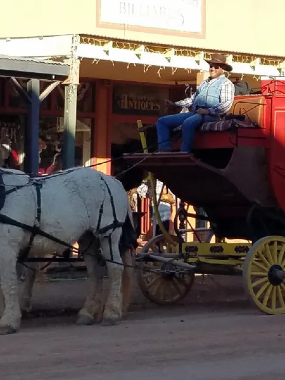 Horse-drawn red stagecoach with a driver on a dirt street.