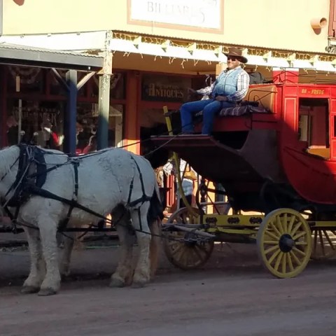 Horse-drawn red stagecoach with a driver on a dirt street.