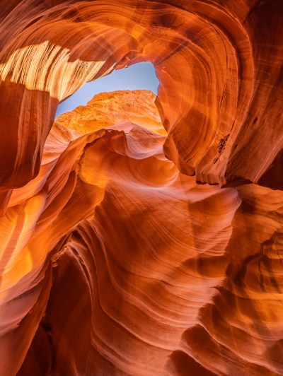 Sunlit red rock formations in a canyon with a visible sky opening.