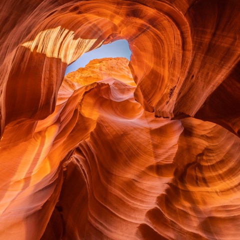 Sunlit red rock formations in a canyon with a visible sky opening.