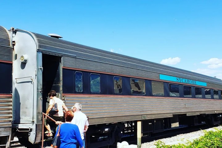 Three people boarding a vintage train under a blue sky.
