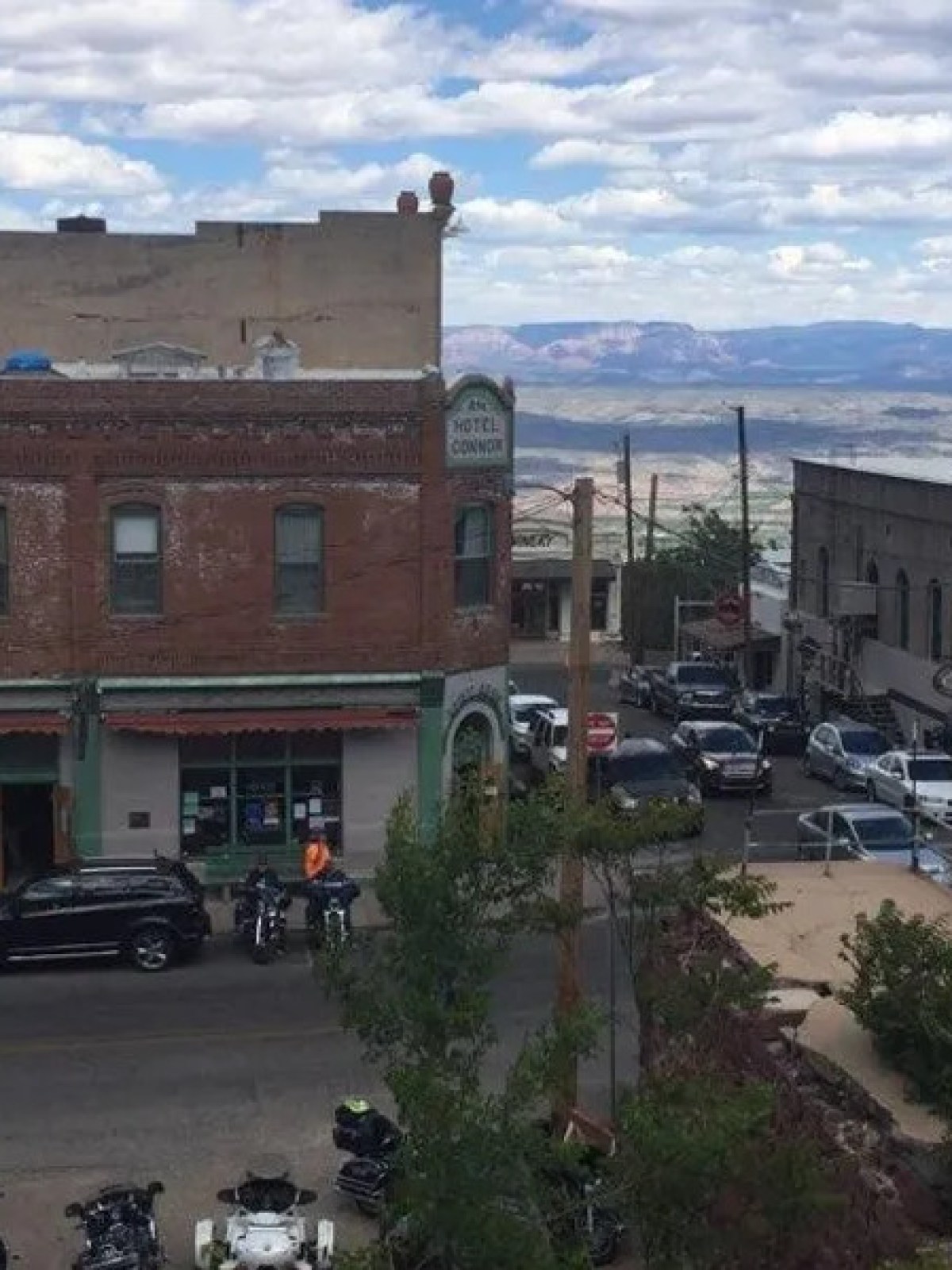 Urban street view with cars and motorcycles, brick buildings, and cloudy skies.