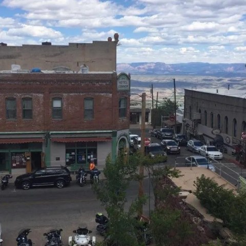 Urban street view with cars and motorcycles, brick buildings, and cloudy skies.