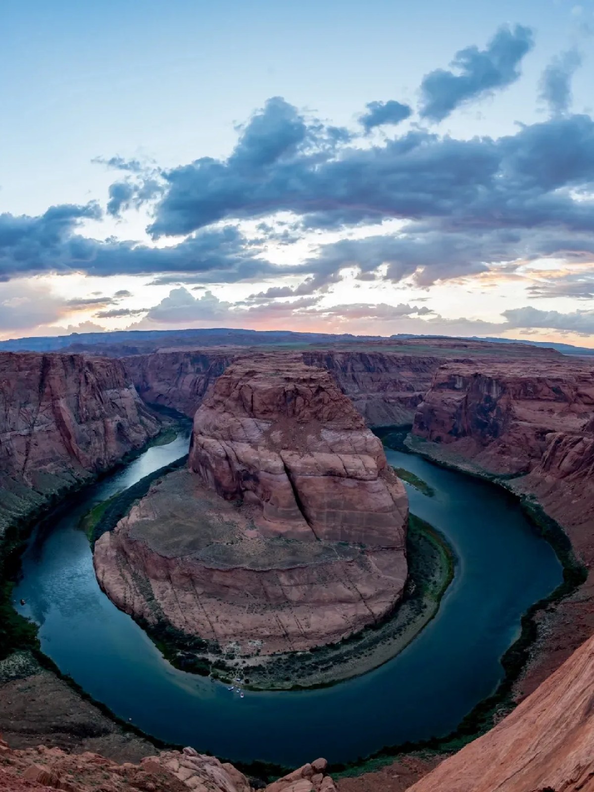 Horseshoe Bend at sunset with a river curving around a sandstone cliff under a cloudy sky.