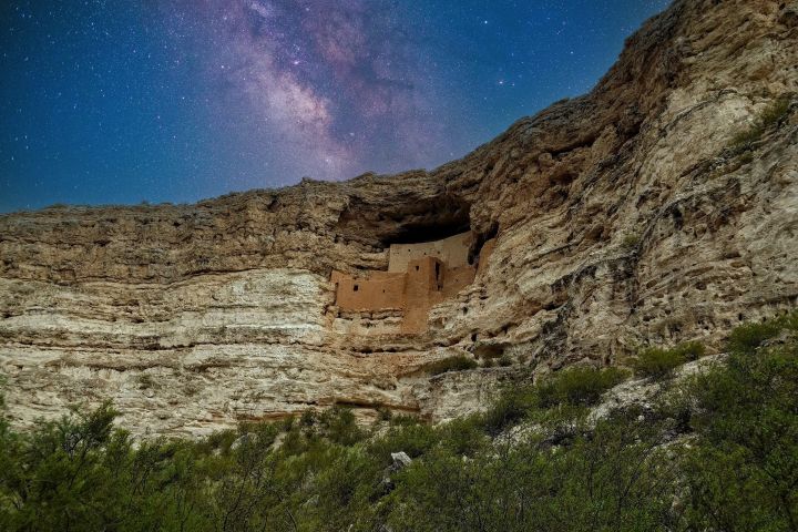 Cliffside ancient dwelling under starry sky and Milky Way.